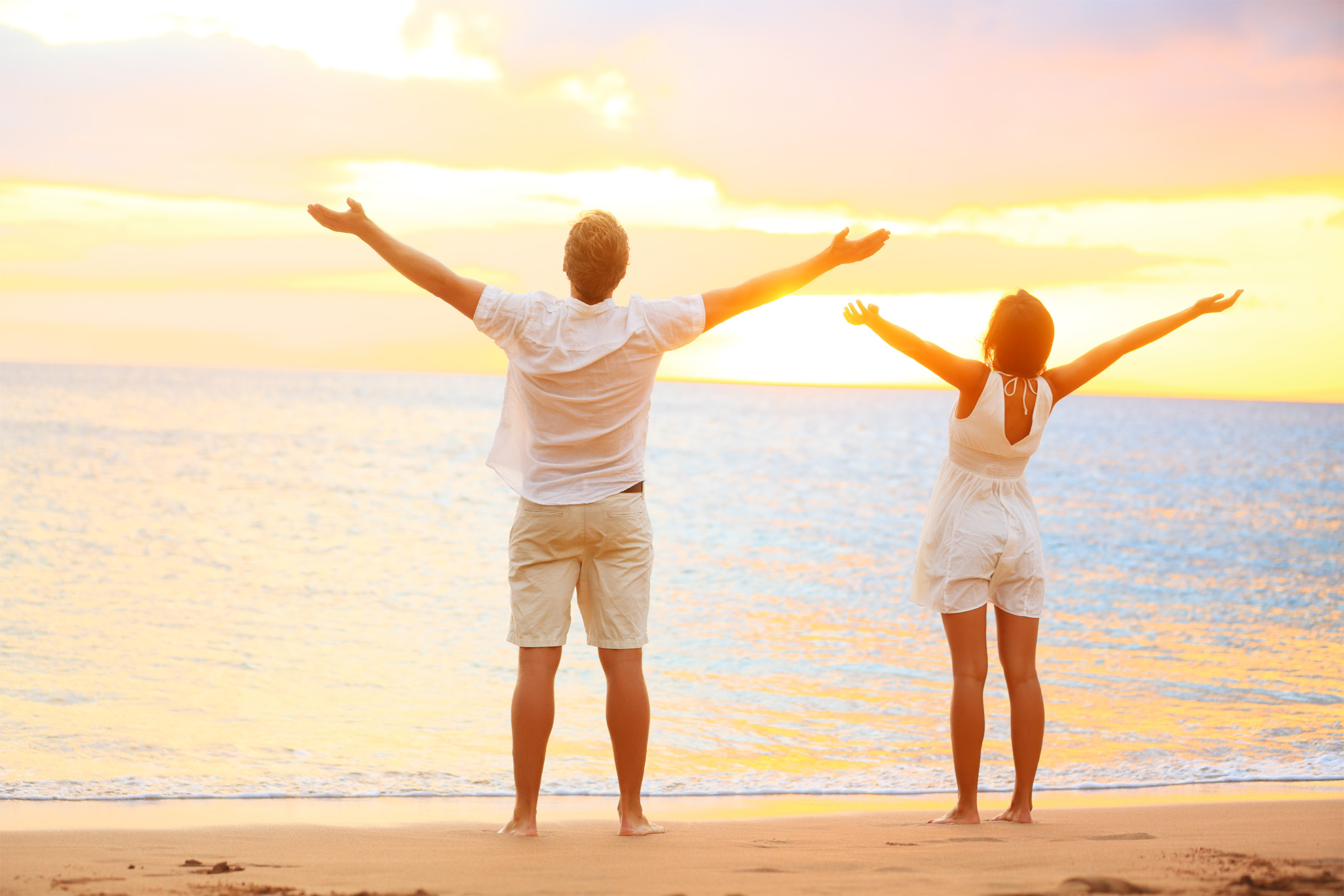 Happy cheering couple enjoying sunset at beach with arms raised up in joyful elated happiness. Happiness concept with young joyous couple, Caucasian man and Asian woman.